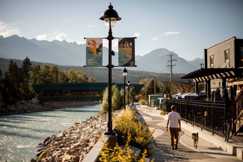 Man walking his dog in late-afternoon light, along a pathway along the Kicking Horse River through town - during the golden hour