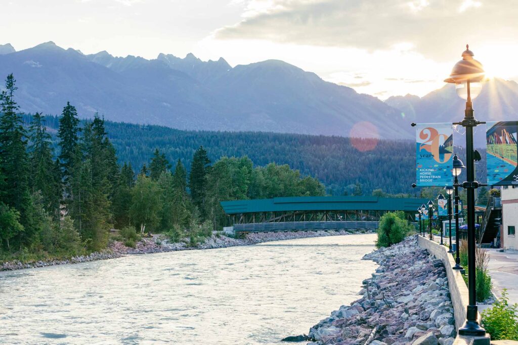 sun setting behind the dogtooth mountain range with the Kicking Horse river in the foreground as it flows under the pedestrian bridge