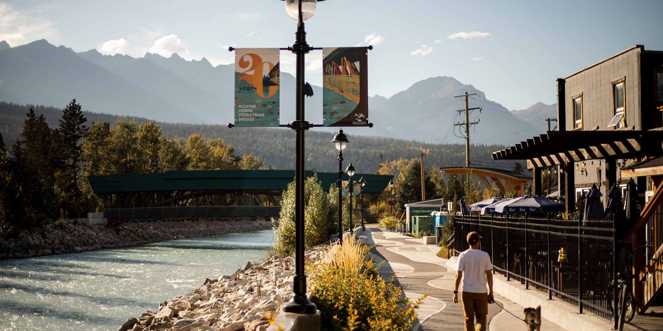 Man walking his dog in late-afternoon light, along a pathway along the Kicking Horse River through town - during the golden hour