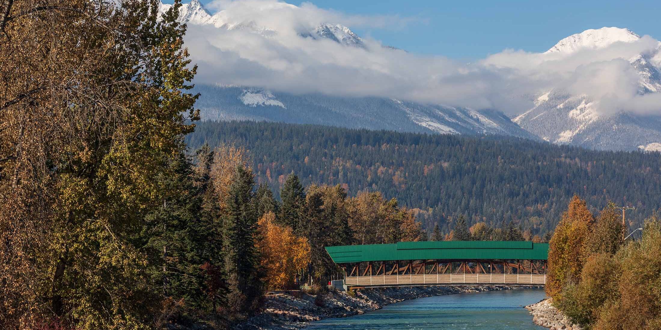 Kicking Horse River under the pedestrian bridge with fall colours and snow-capped peaks of the dogtooth range